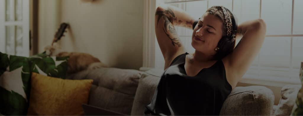 Person relaxing on a couch with headphones, eyes closed, possibly listening to music or a podcast