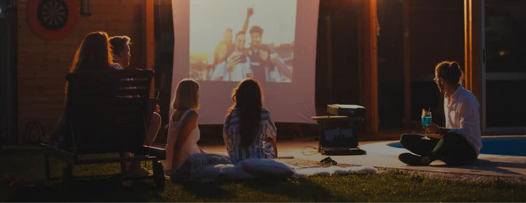 People watching a movie projected outdoors in a backyard at night