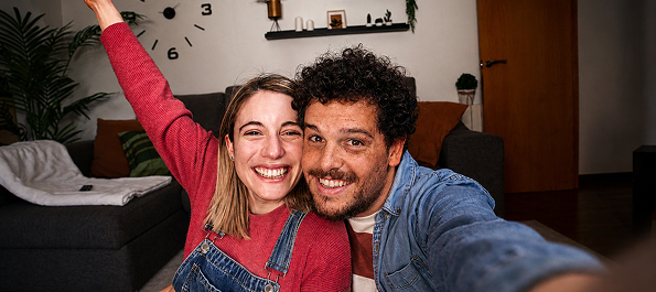 A smiling couple takes a selfie, the woman raising an arm in celebration