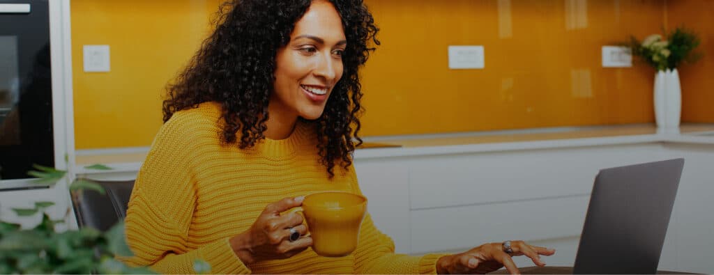 Smiling woman in a yellow sweater using a laptop and holding a mug