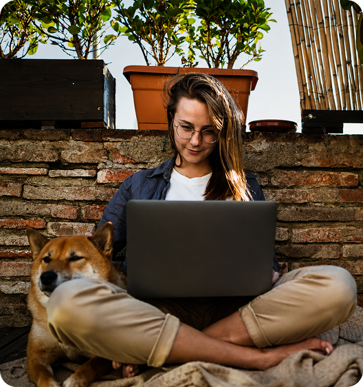 A woman works on a laptop outdoors with her dog beside her
