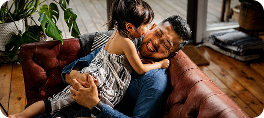 Father and child embracing on a couch, smiling and laughing
