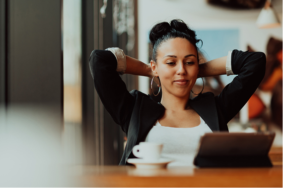 Woman relaxed and smiling while looking at a tablet with a cup of coffee nearby