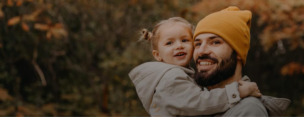 Smiling man holding a happy child against a blurred outdoor background