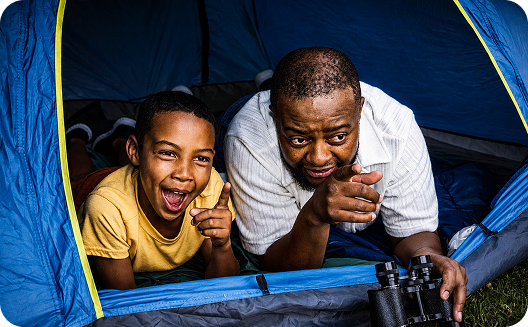 Father and son excitedly pointing forward from inside a tent, with binoculars nearby