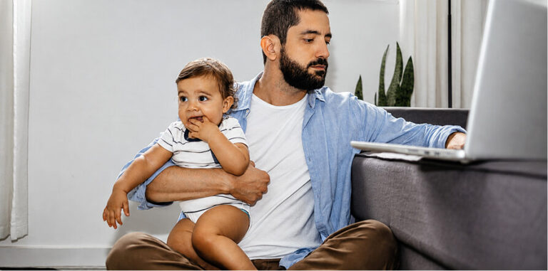 Man working on laptop with baby on his lap