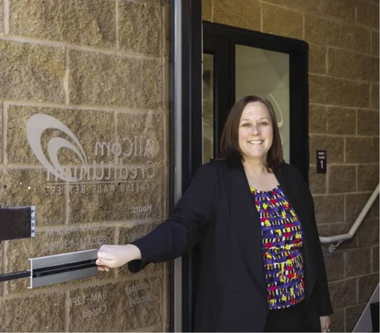 Woman smiling in an open doorway with a business logo on the glass