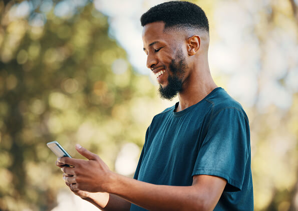 Smiling man looking down at his phone outdoors