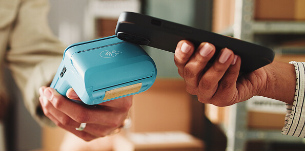 A smartphone tapping on a blue payment terminal with a contactless payment symbol