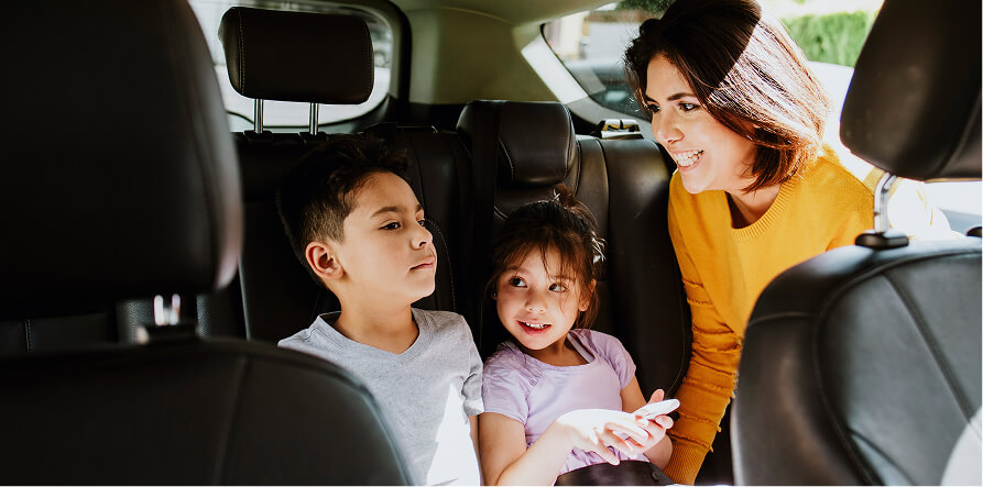 Woman in front seat looking back and smiling at two children in car's back seat