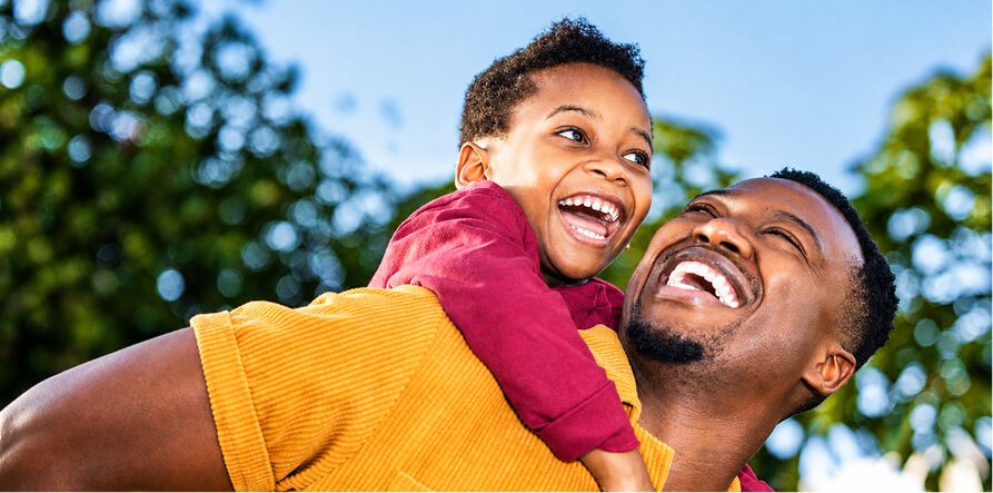 Father and child laughing together, with the child on the father's back