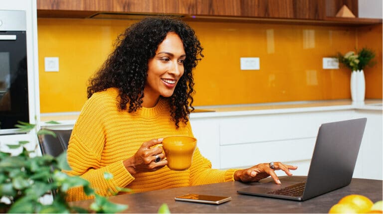 Woman smiling while using a laptop and holding a mug
