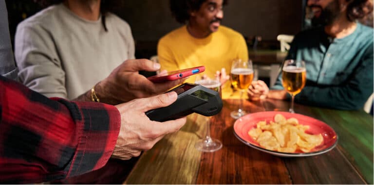 A person uses a smartphone to make a contactless payment at a table with friends and drinks