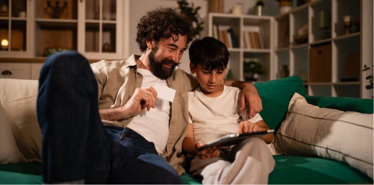 Man holding a credit card and boy looking at a tablet on a couch