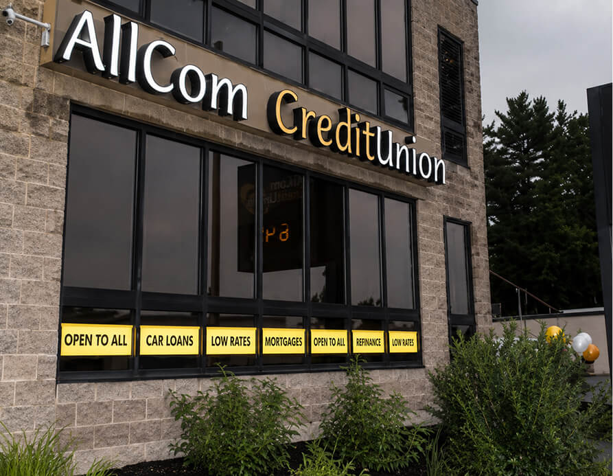 Exterior of AllCom Credit Union building with banners: Open to All, Car Loans, Low Rates, Mortgages, Refinance