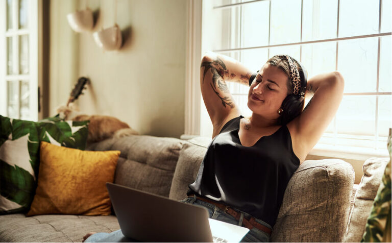 Person relaxing on a couch with headphones, eyes closed, a laptop nearby