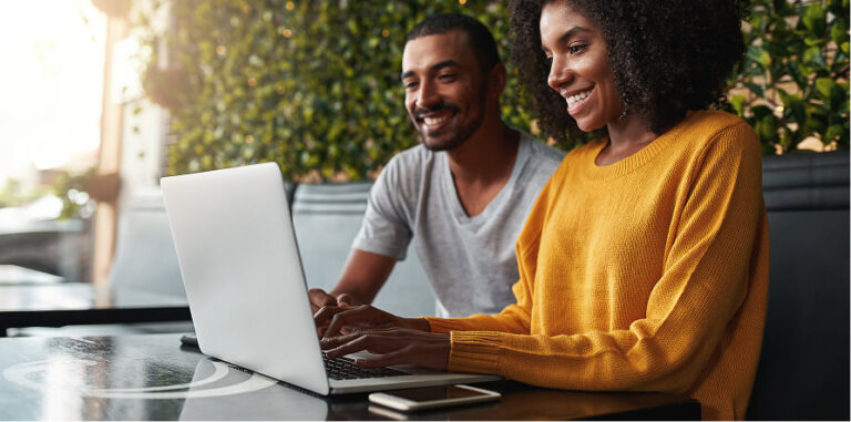 Two smiling people, a man and a woman, look at a laptop and type