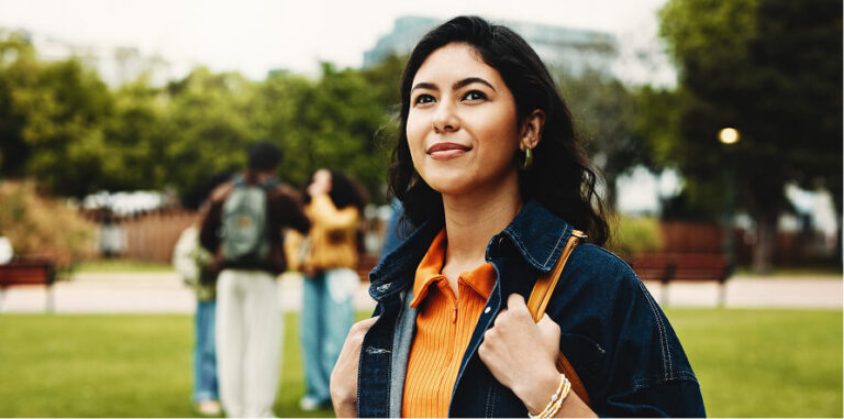 Smiling young woman looking up, standing in a park with blurred people in the background