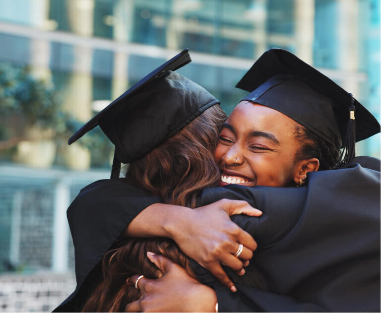 Two graduates in caps and gowns hugging joyfully