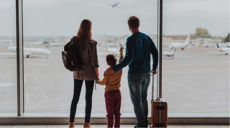 Family with a child looking out airport window at a plane taking off