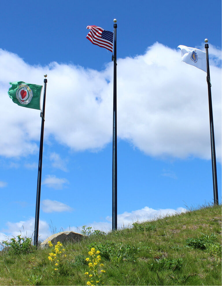 Flags of History Matters, USA, and Massachusetts flying on poles against a blue sky