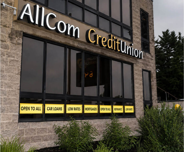 Exterior of AllCom CreditUnion building with signs for "OPEN TO ALL," "CAR LOANS," "LOW RATES," "MORTGAGES," and "REFINANCE"