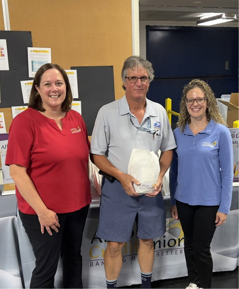 Two women in AllCom Credit Union shirts with a man holding a gift bag