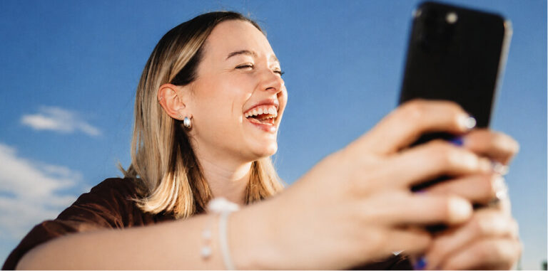 Smiling woman holding a smartphone, looking at the screen and laughing