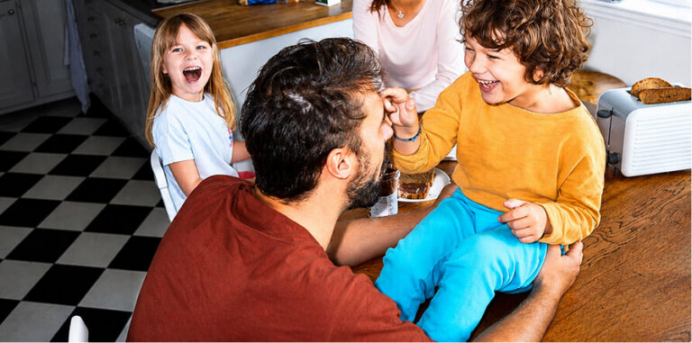 Father and two young children laughing together at a kitchen counter