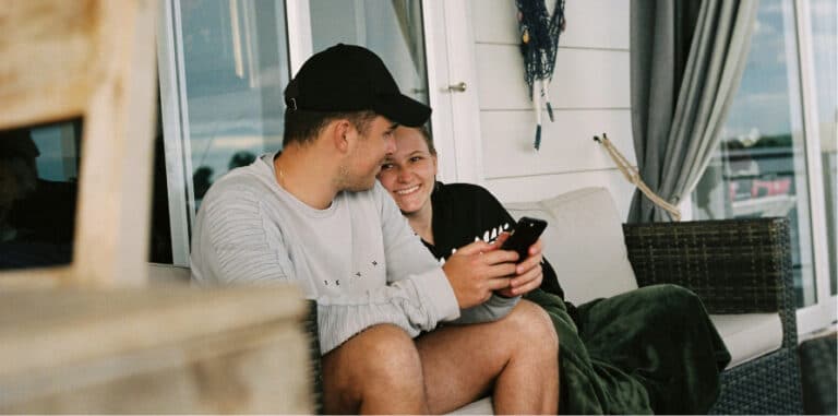 Man and woman sitting together on a couch looking at a phone, the woman smiling
