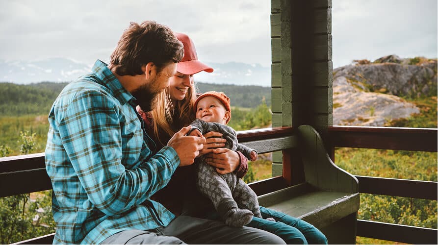 Parents smiling at their happy baby on a porch with a mountain view