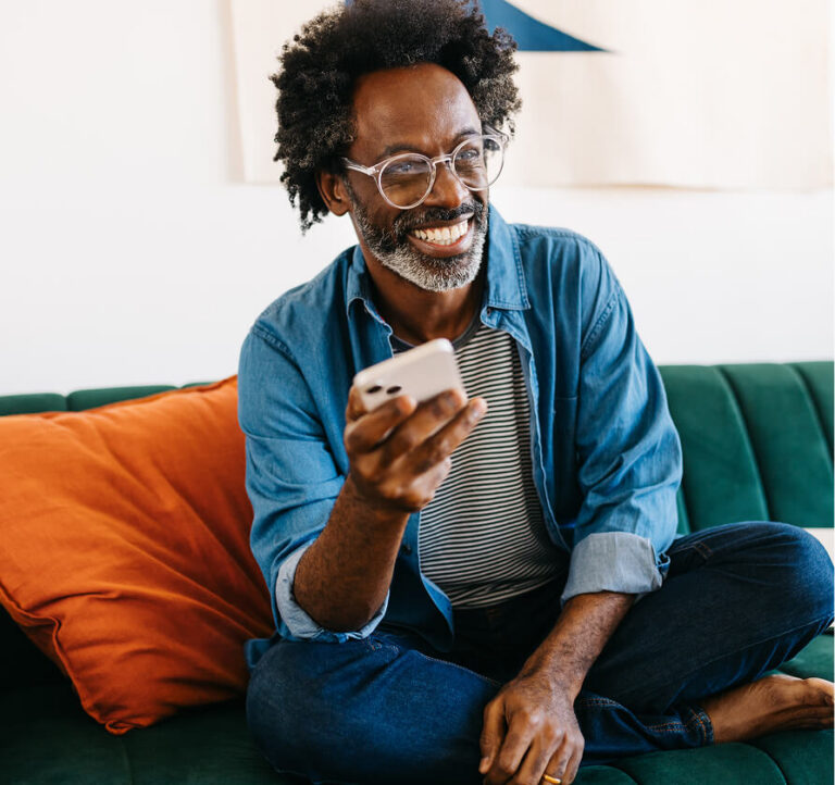 Man with glasses smiling while looking at his smartphone on a green couch