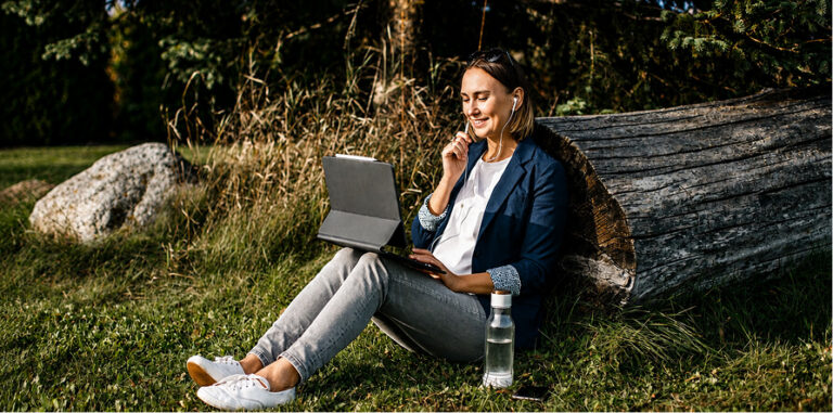 Woman sitting outside, leaning on a log, using a tablet and earbuds
