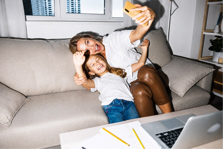 Happy woman and girl take a selfie on a couch, a laptop on the table nearby