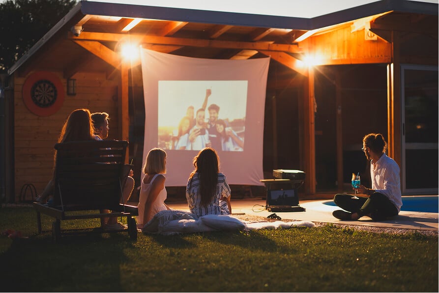 Friends watching an outdoor movie projection on a screen in a backyard