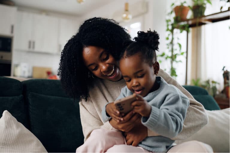 A smiling adult and a child sitting together, both looking at a smartphone held by the child