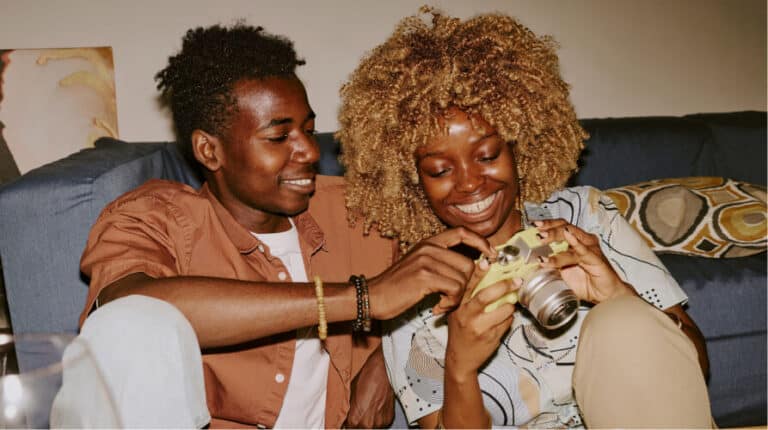 Two smiling young adults looking at a digital camera together on a couch