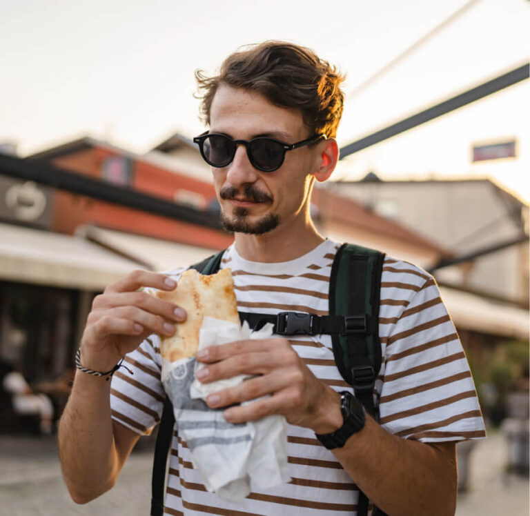 Man in sunglasses and striped shirt eating a sandwich outdoors